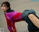 A woman in a colorful jacket and skirt doing a handstand on the ground.