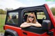 A woman sitting in the driver's seat of a red jeep.