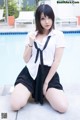 A woman in a white shirt and black skirt posing by a pool.