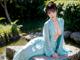 A woman in a blue kimono sitting on a rock by a pond.