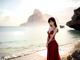 A woman in a red dress standing on a beach.